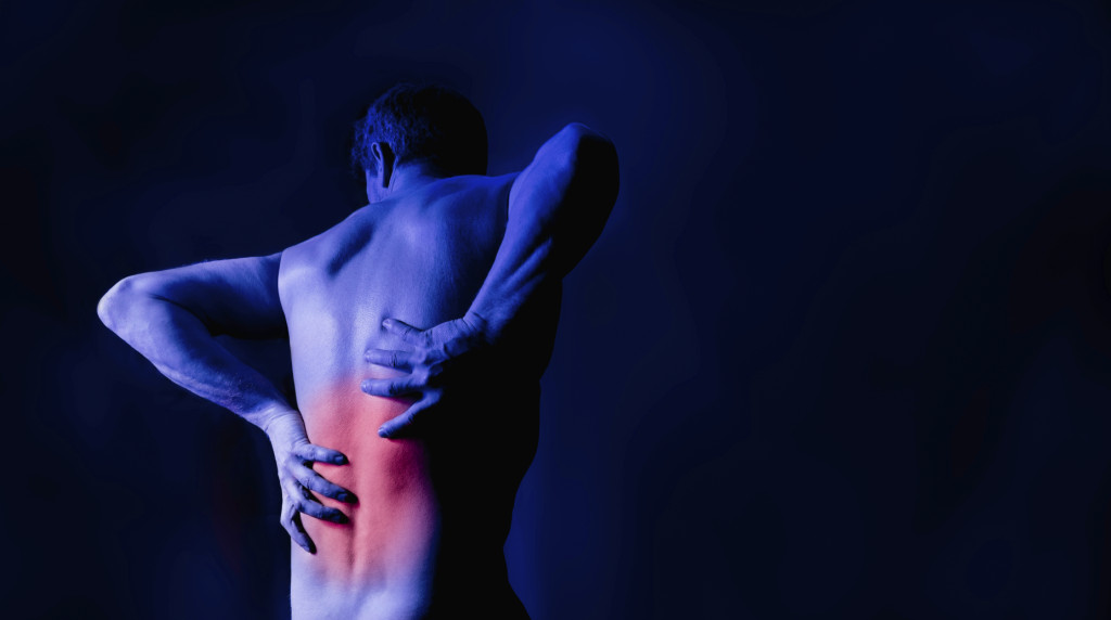 A man holding his back in pain. Studio shot with red marking the area of pain.
